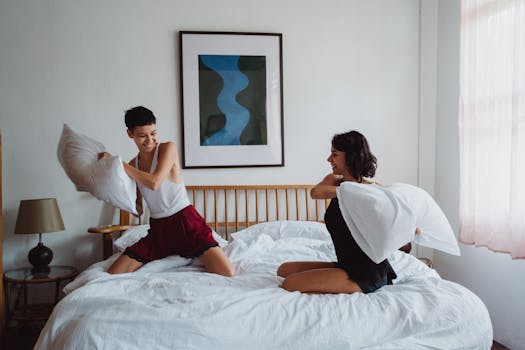 A joyful moment of two women enjoying a pillow fight on a bed, capturing playful love and togetherness.