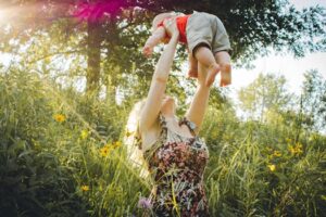 A joyful mother lifts her baby in a sunny summer meadow, capturing a moment of love and happiness.