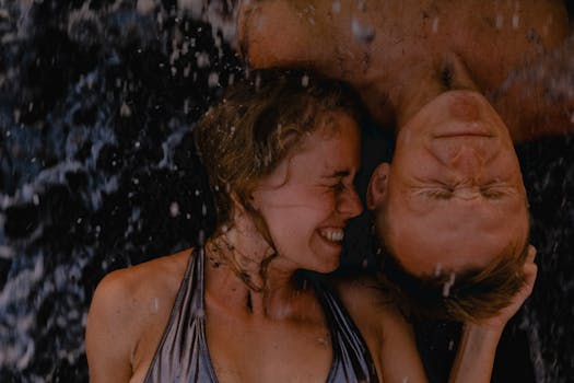 Joyful couple embracing beach waves, eyes closed, under summer sun.