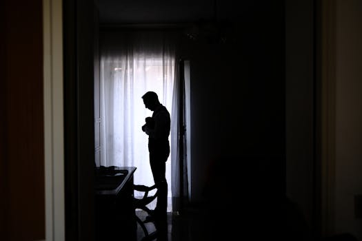Shadowy silhouette of a father holding his baby in a dimly lit room, creating an intimate moment.